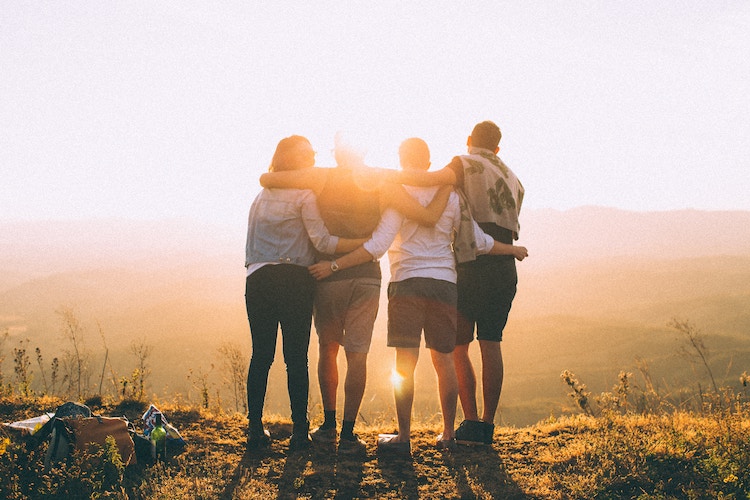 Four people huddling
   together looking to the sunset.