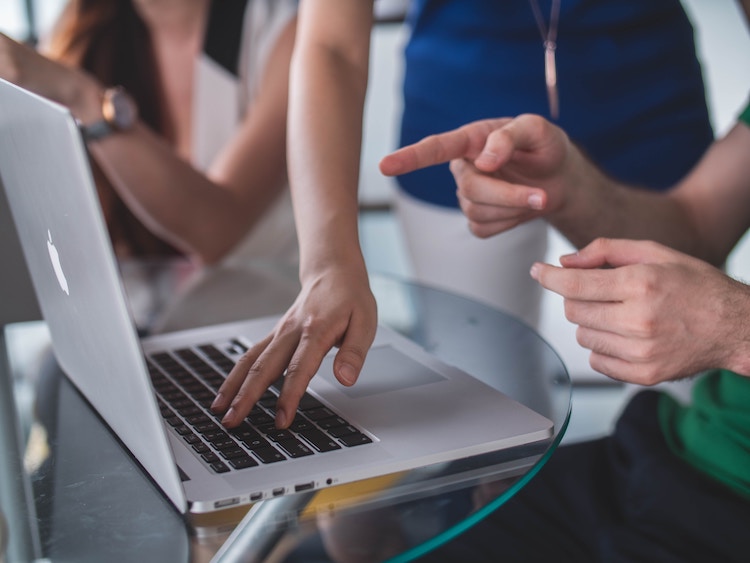 Two people chatting behind a MacBook Pro